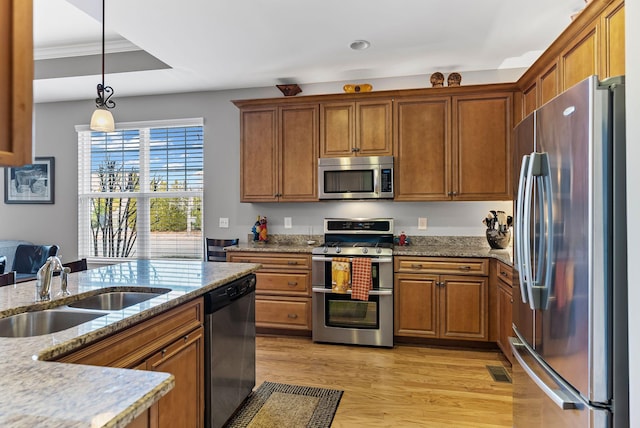 kitchen with sink, hanging light fixtures, stainless steel appliances, light hardwood / wood-style floors, and light stone countertops