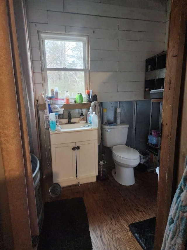 bathroom featuring toilet, wood-type flooring, wooden walls, and vanity