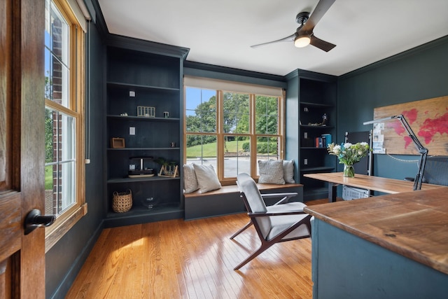 office featuring crown molding, built in shelves, ceiling fan, and light wood-type flooring