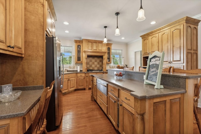 kitchen featuring appliances with stainless steel finishes, backsplash, light hardwood / wood-style floors, a kitchen island, and decorative light fixtures