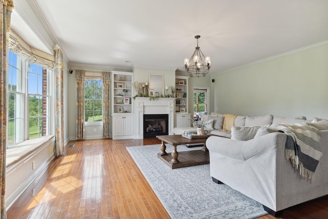 living room with an inviting chandelier, hardwood / wood-style floors, crown molding, and built in features