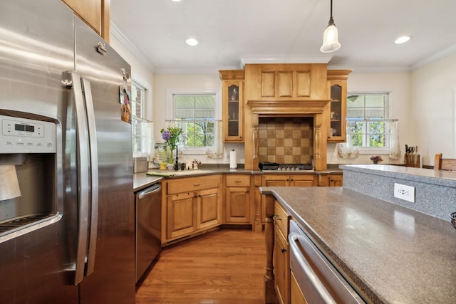 kitchen with appliances with stainless steel finishes, pendant lighting, backsplash, ornamental molding, and light hardwood / wood-style floors