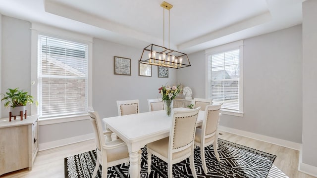 dining area with a raised ceiling, a wealth of natural light, a notable chandelier, and light hardwood / wood-style floors