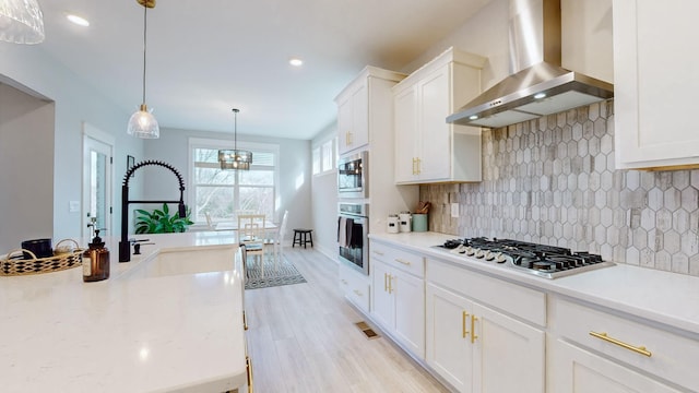 kitchen featuring white cabinetry, hanging light fixtures, wall chimney exhaust hood, and appliances with stainless steel finishes