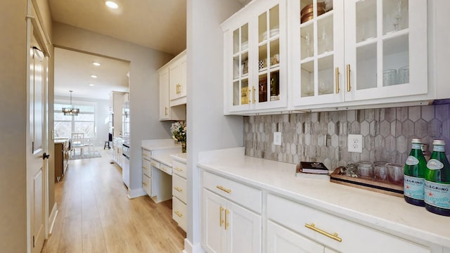 bar featuring white cabinetry, an inviting chandelier, light wood-type flooring, light stone countertops, and backsplash