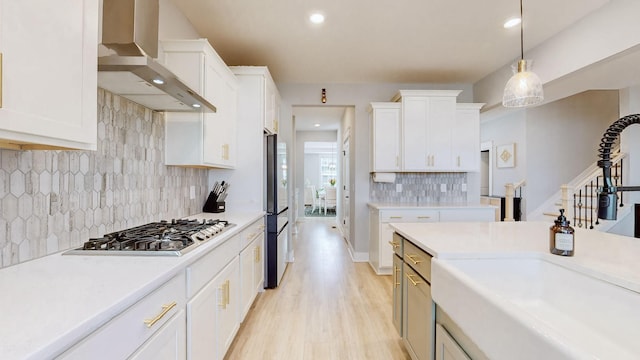 kitchen featuring white cabinets, decorative light fixtures, stainless steel gas cooktop, and wall chimney range hood