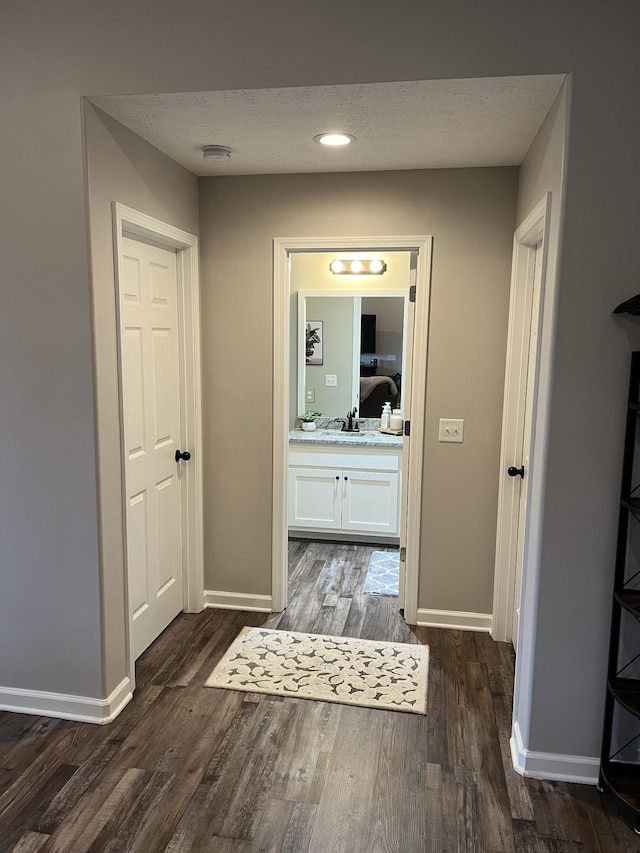 corridor with sink, dark wood-type flooring, and a textured ceiling