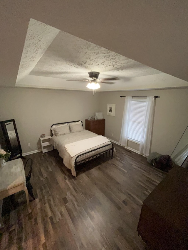 bedroom with ceiling fan, dark hardwood / wood-style flooring, a raised ceiling, and a textured ceiling