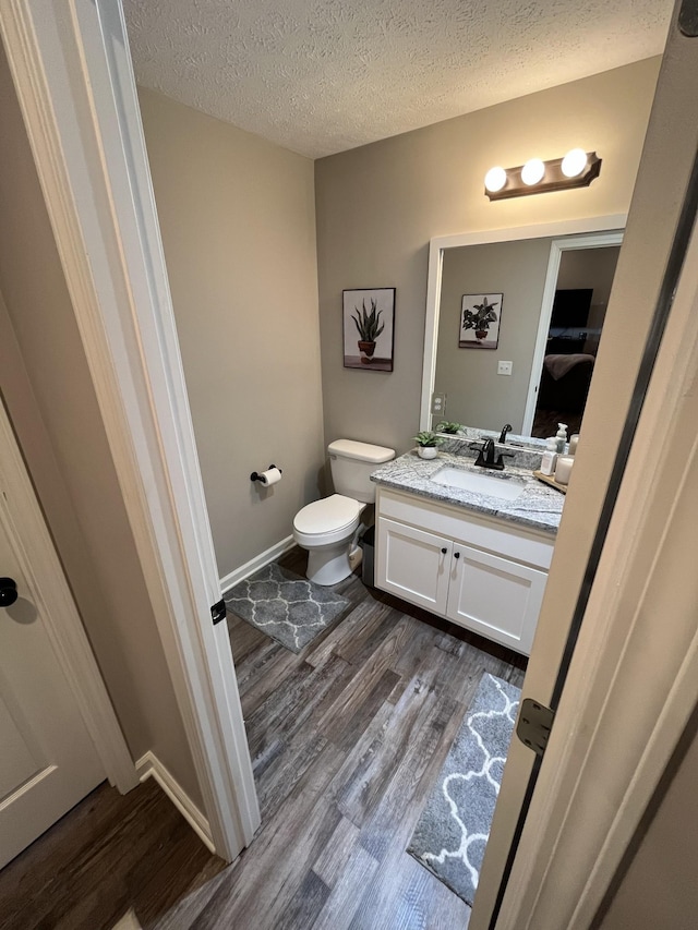 bathroom featuring hardwood / wood-style flooring, vanity, toilet, and a textured ceiling