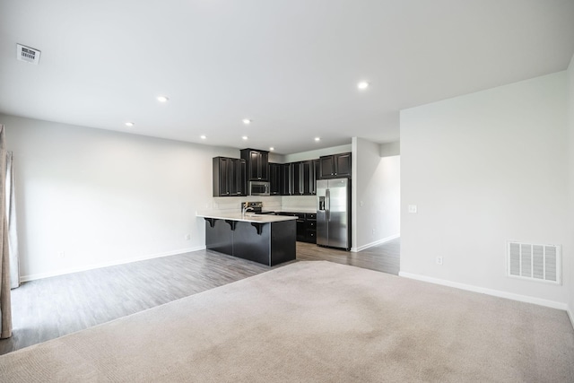 kitchen featuring a kitchen island with sink, wood-type flooring, stainless steel appliances, and a breakfast bar