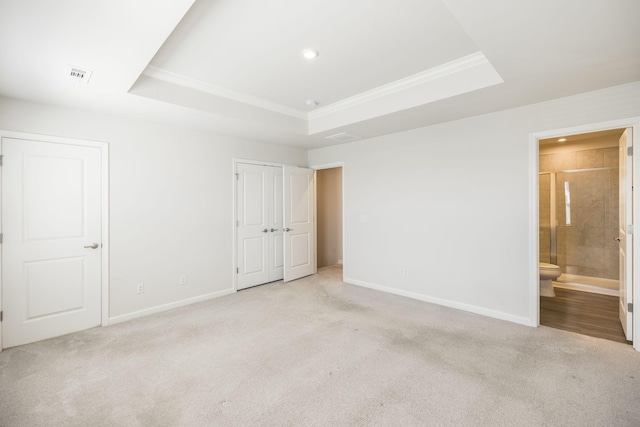 unfurnished bedroom with connected bathroom, light colored carpet, and a raised ceiling