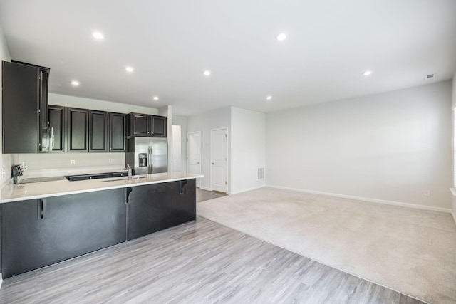 kitchen featuring stainless steel refrigerator with ice dispenser, a breakfast bar, sink, light wood-type flooring, and kitchen peninsula