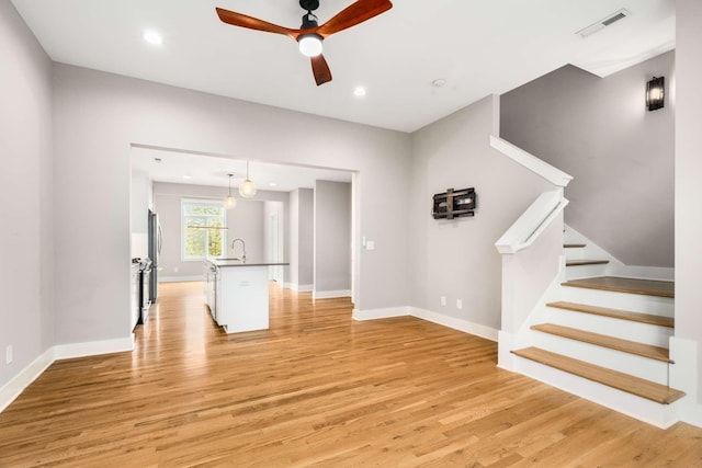 unfurnished living room featuring ceiling fan, sink, and light wood-type flooring