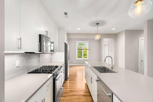 kitchen featuring sink, hanging light fixtures, stainless steel appliances, decorative backsplash, and white cabinets