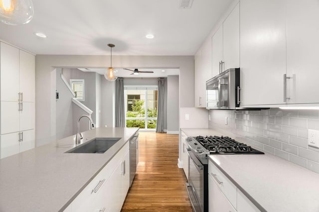 kitchen with appliances with stainless steel finishes, pendant lighting, white cabinetry, sink, and decorative backsplash