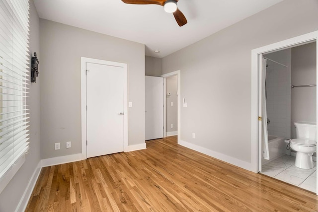 unfurnished bedroom featuring ceiling fan, ensuite bath, multiple windows, and light wood-type flooring