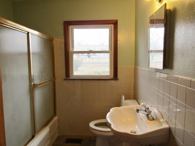 full bathroom featuring toilet, bath / shower combo with glass door, sink, and tile walls