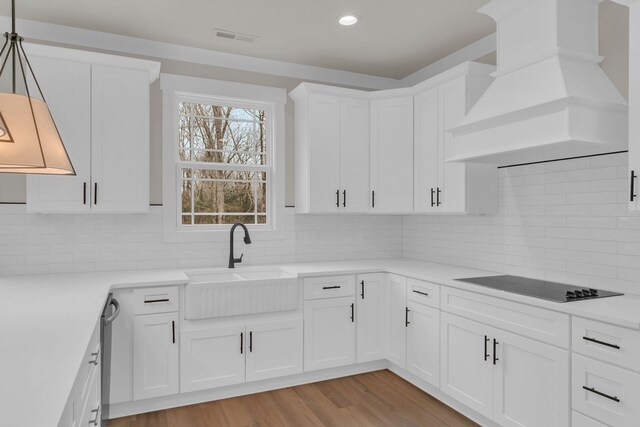 kitchen featuring sink, custom exhaust hood, decorative light fixtures, black electric stovetop, and white cabinets