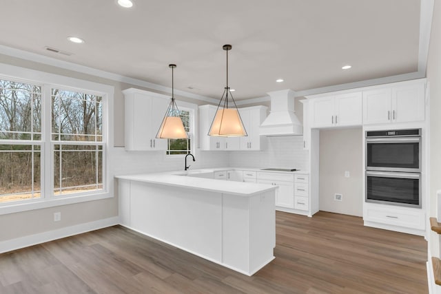 kitchen featuring double oven, decorative light fixtures, white cabinets, kitchen peninsula, and custom range hood