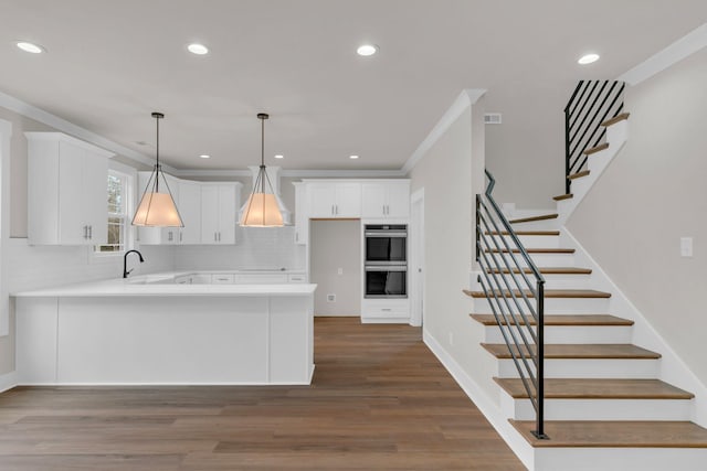 kitchen featuring sink, kitchen peninsula, pendant lighting, stainless steel double oven, and white cabinets