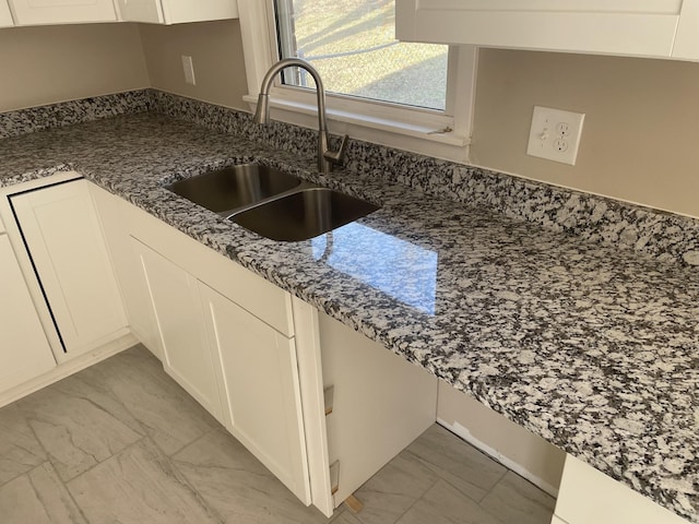 kitchen with a sink, stone counters, marble finish floor, and white cabinetry