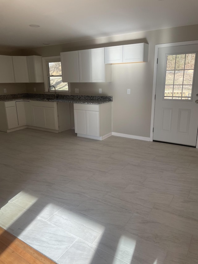 kitchen with a sink, baseboards, dark stone countertops, and white cabinetry