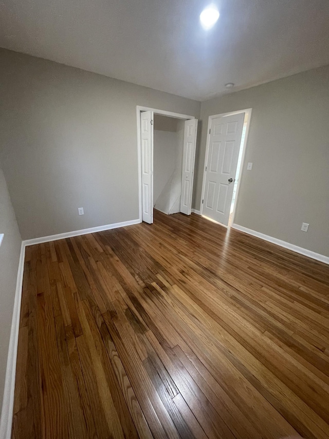 unfurnished bedroom featuring dark wood finished floors, a closet, and baseboards