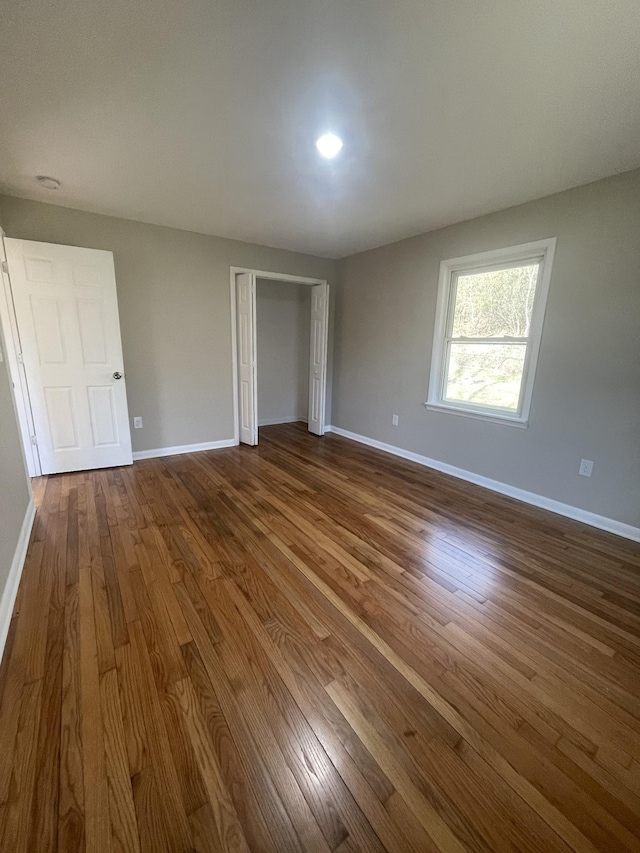 unfurnished bedroom featuring dark wood-style floors, a closet, and baseboards