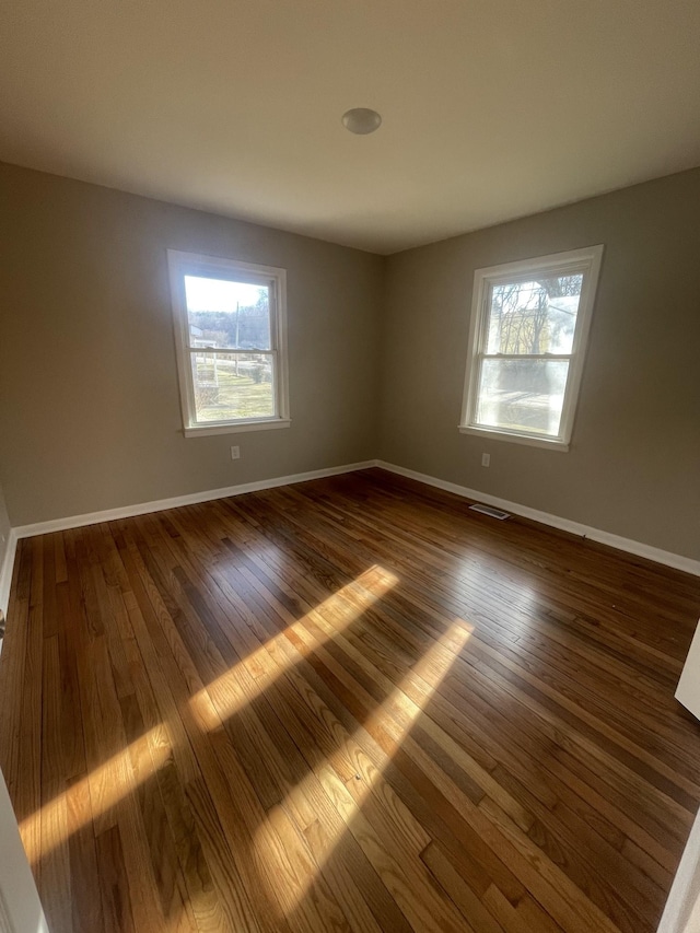 spare room featuring visible vents, baseboards, a healthy amount of sunlight, and dark wood finished floors