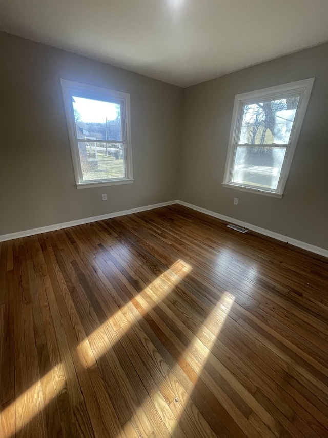 empty room featuring visible vents, plenty of natural light, and dark wood finished floors