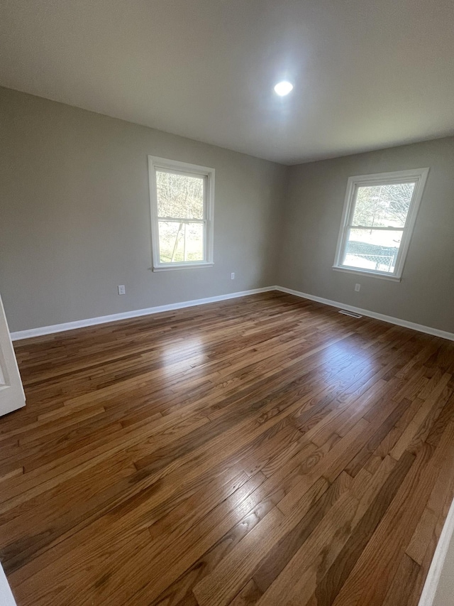 unfurnished room featuring a healthy amount of sunlight, dark wood-type flooring, and baseboards