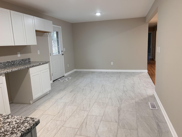 kitchen with stone counters, visible vents, built in desk, and white cabinetry