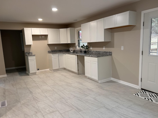 kitchen featuring white cabinets, baseboards, and a sink