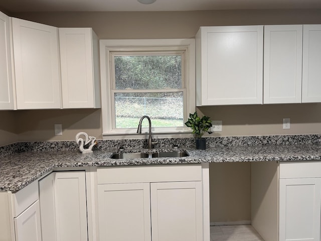 kitchen featuring a sink, light stone countertops, and white cabinetry