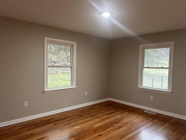 unfurnished room featuring hardwood / wood-style flooring, baseboards, and visible vents