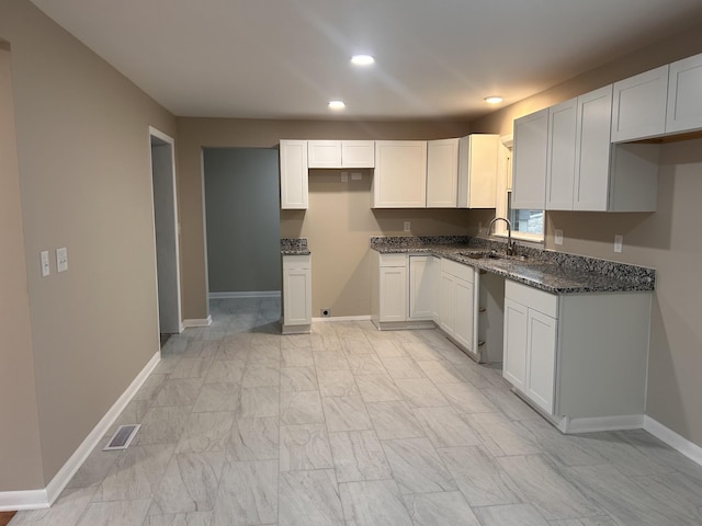 kitchen featuring visible vents, a sink, recessed lighting, dark stone counters, and baseboards