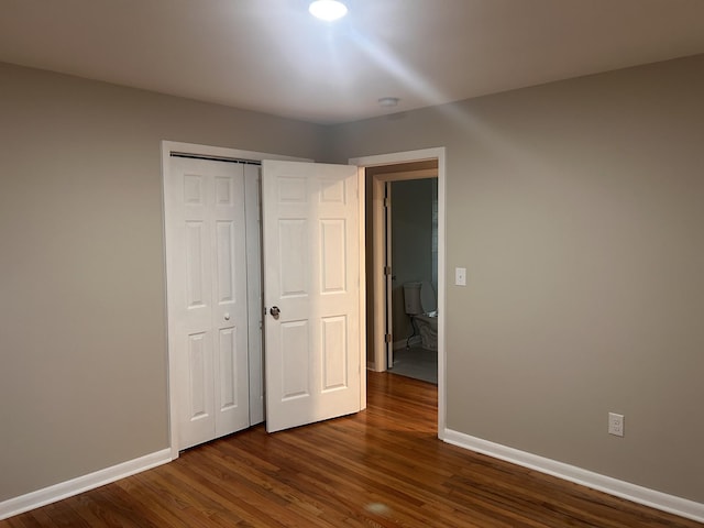 unfurnished bedroom featuring baseboards, dark wood-style flooring, and a closet