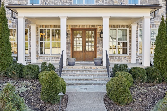 view of exterior entry featuring stone siding, covered porch, and french doors