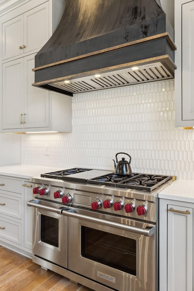 kitchen with custom exhaust hood, tasteful backsplash, white cabinetry, light wood-type flooring, and range with two ovens