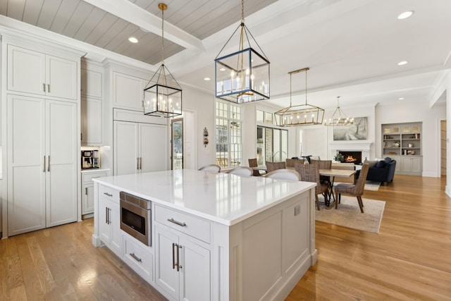 kitchen featuring beam ceiling, a center island, built in appliances, white cabinets, and decorative light fixtures