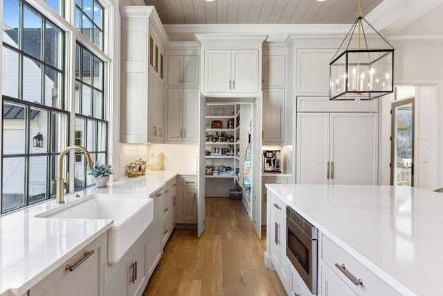 kitchen featuring pendant lighting, sink, light hardwood / wood-style flooring, stainless steel microwave, and white cabinets