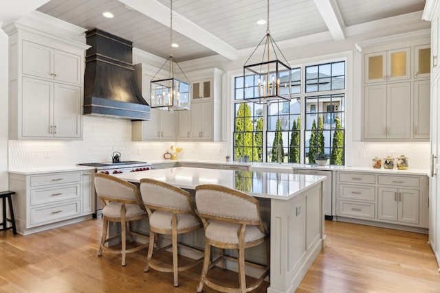 kitchen with a notable chandelier, pendant lighting, custom range hood, a kitchen island, and beamed ceiling