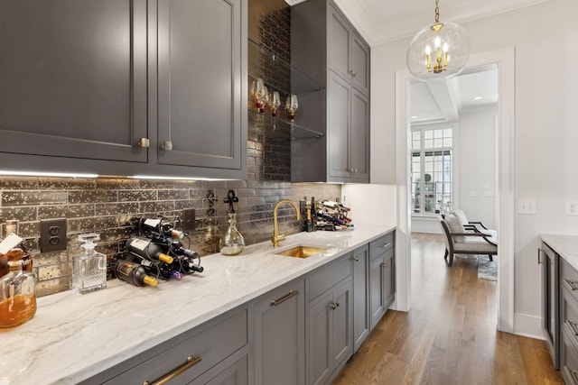 bar featuring hanging light fixtures, light stone countertops, sink, and gray cabinetry