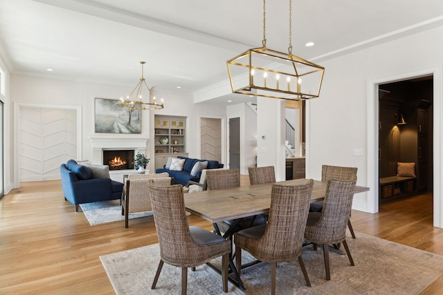 dining room with ornamental molding, built in features, a chandelier, and light wood-type flooring