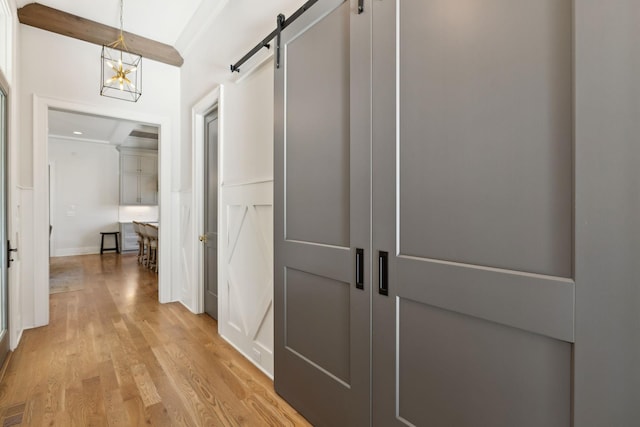 corridor featuring a barn door, beamed ceiling, and light wood-type flooring