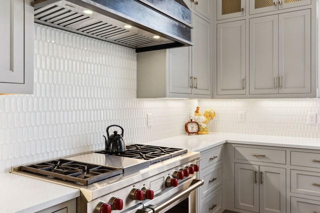 kitchen featuring decorative backsplash, wall chimney exhaust hood, high end stove, and gray cabinetry