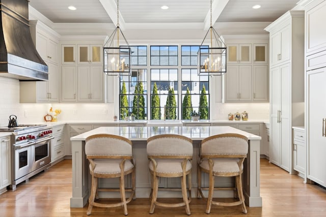 kitchen featuring custom exhaust hood, a center island, a notable chandelier, beamed ceiling, and range with two ovens