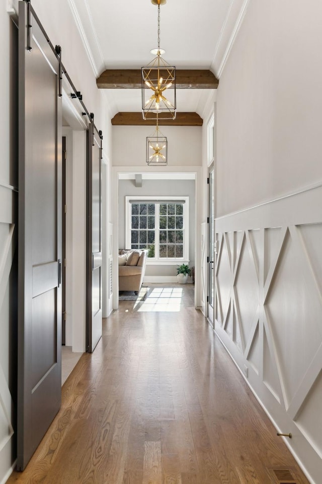 corridor featuring hardwood / wood-style flooring, a barn door, a chandelier, and crown molding