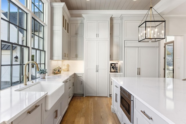 kitchen featuring sink, light hardwood / wood-style flooring, white cabinetry, stainless steel microwave, and decorative light fixtures