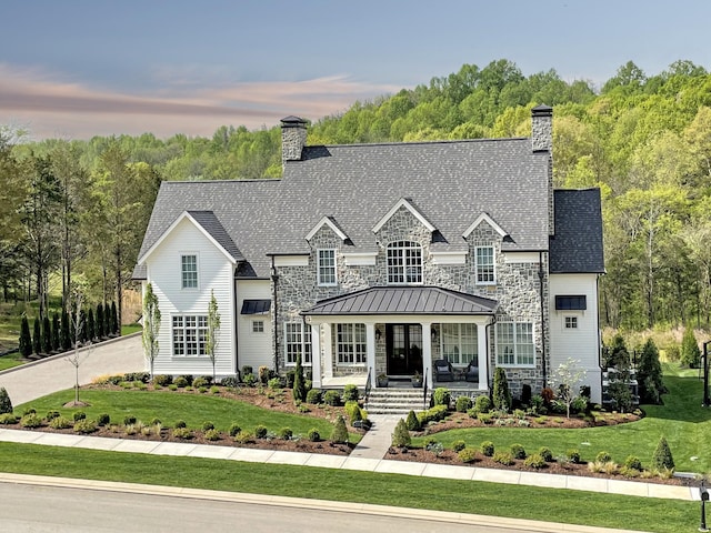 view of front facade with a standing seam roof, a porch, a chimney, and a front yard